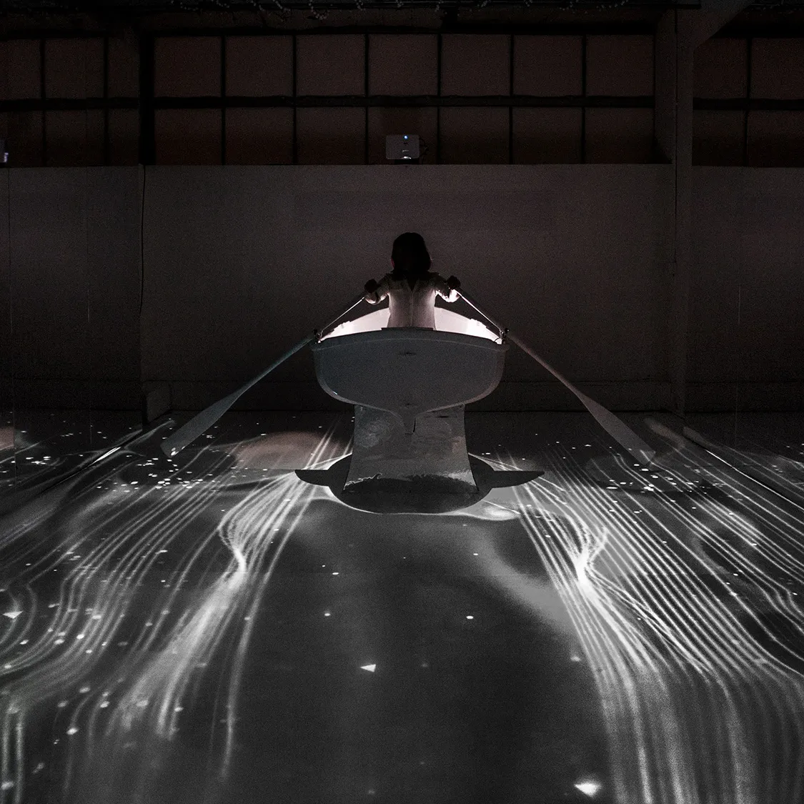 image of woman in rowboat interacting with digital stars and water projections all around her