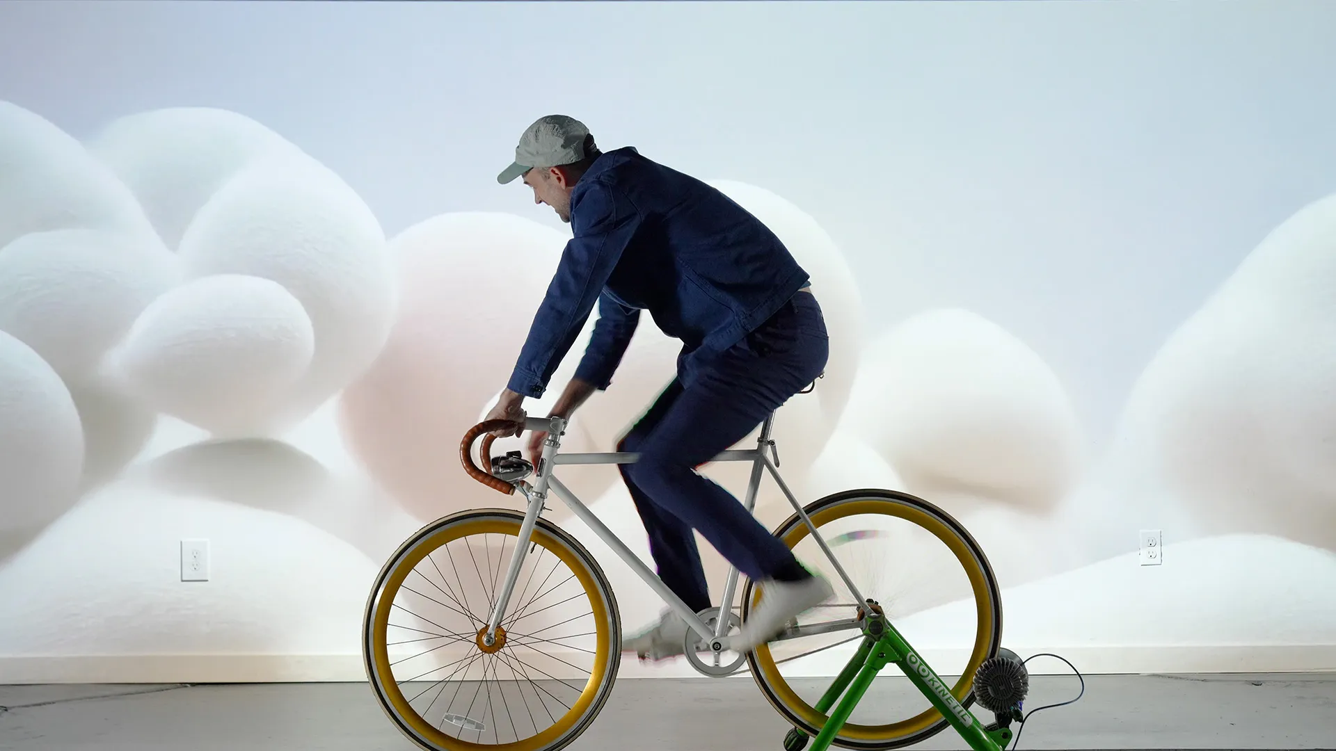 Interactive art installation with a stationary bike connected to a digital screen displaying ai generated abstract graphics that change in response to the cyclist's movements, set in a dark environment with a futuristic, immersive atmosphere. The graphics depict white fluffy cotton balls on a light background.