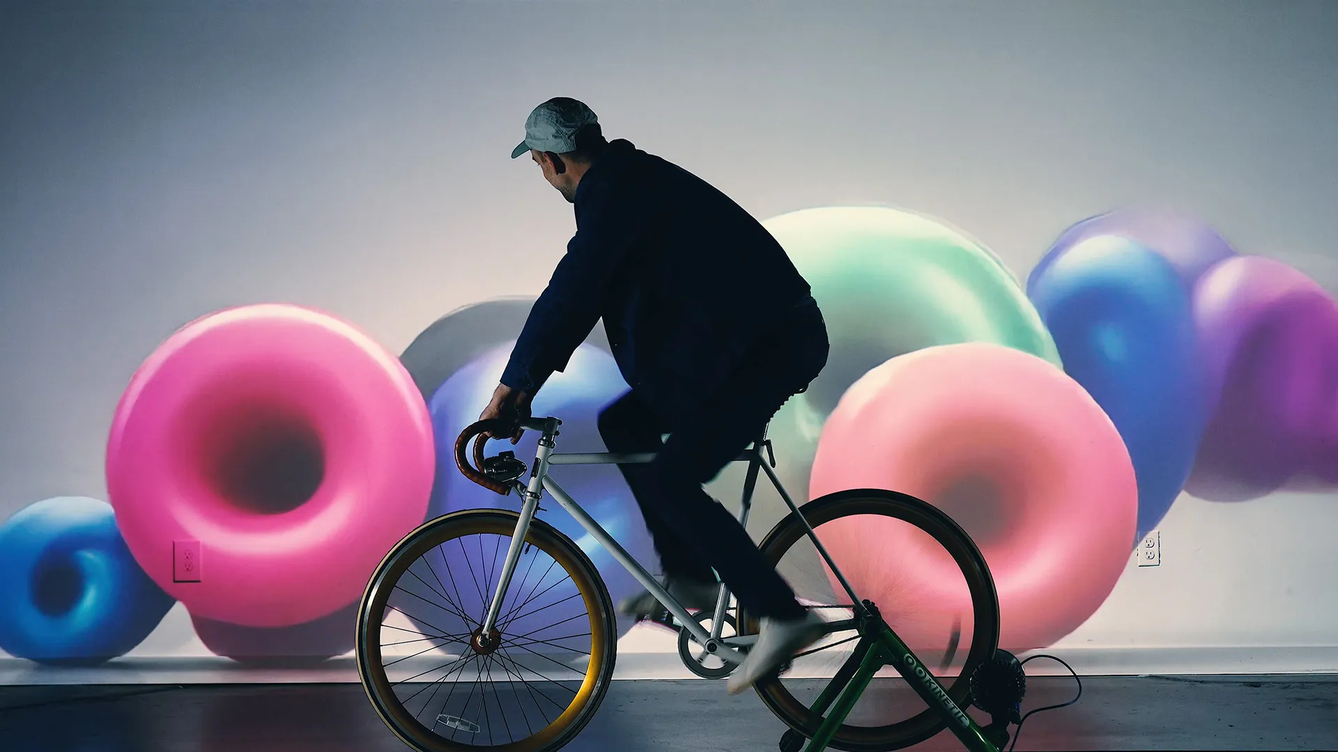 Interactive art installation with a stationary bike connected to a digital screen displaying ai generated abstract graphics that change in response to the cyclist's movements. The graphics show shiny, colorful donut shapes.