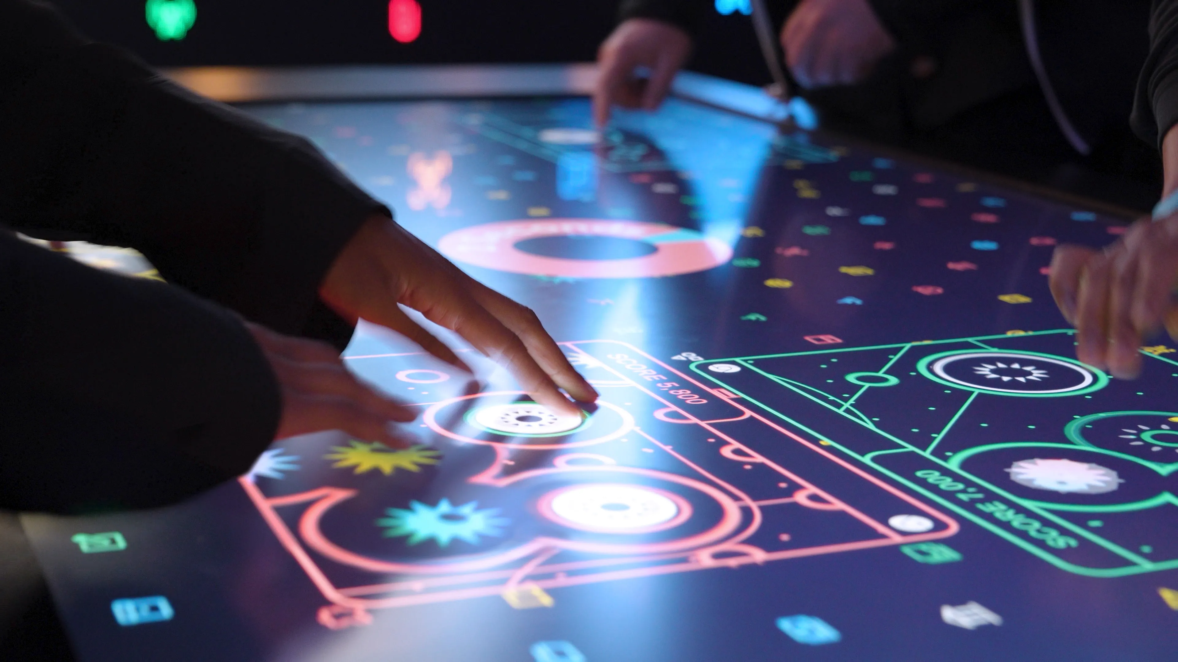 A close-up captures the hands of Bloomberg Technology Summit attendees as they engage with the vibrant Data Defense Game on a touch table. The screen displays stylized Google Chrome windows, where files are actively being scanned for threats.