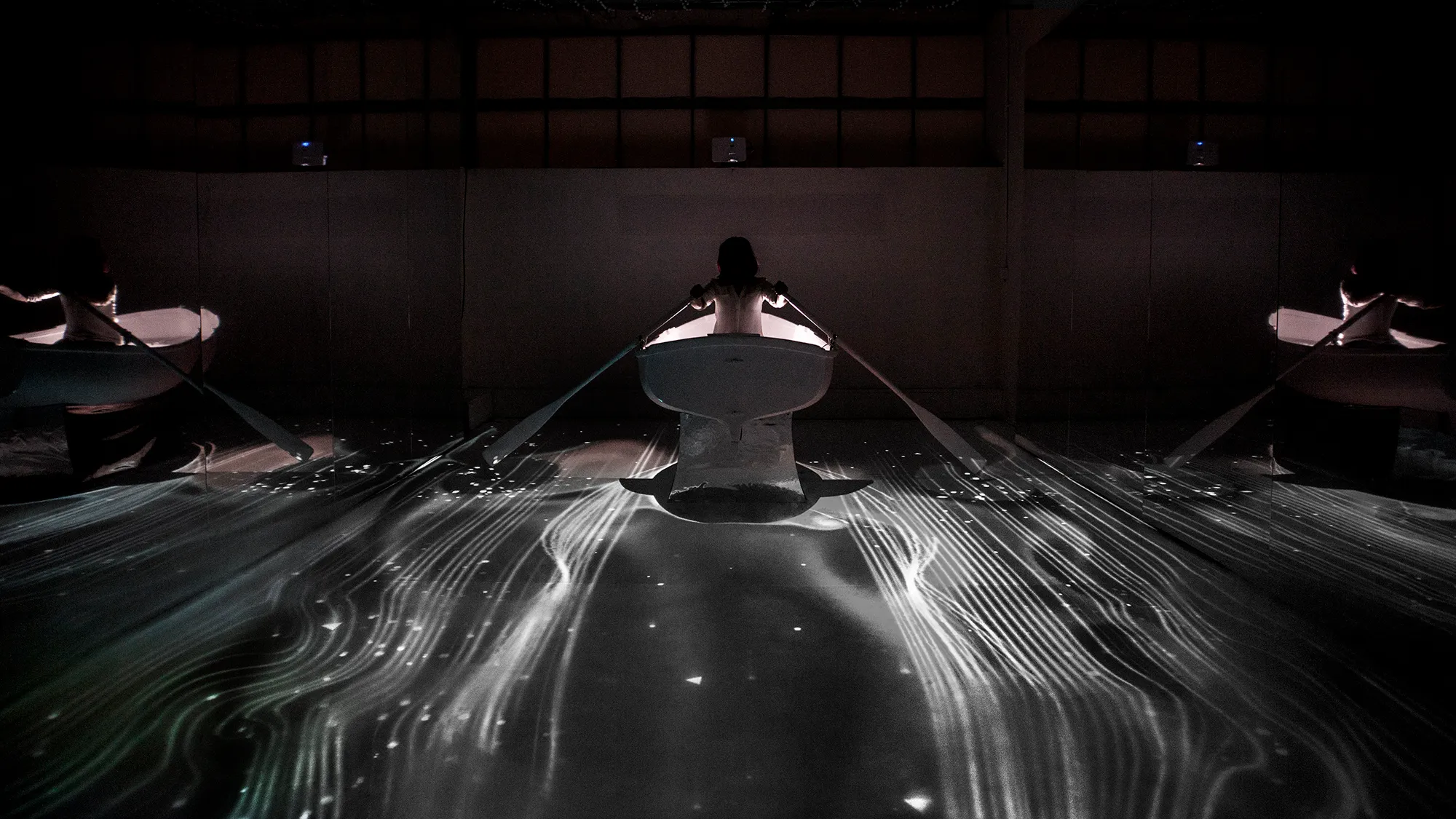 A girld in a boat, rowing through magical, floor projected graphics that are influenced by fluid dynamics.