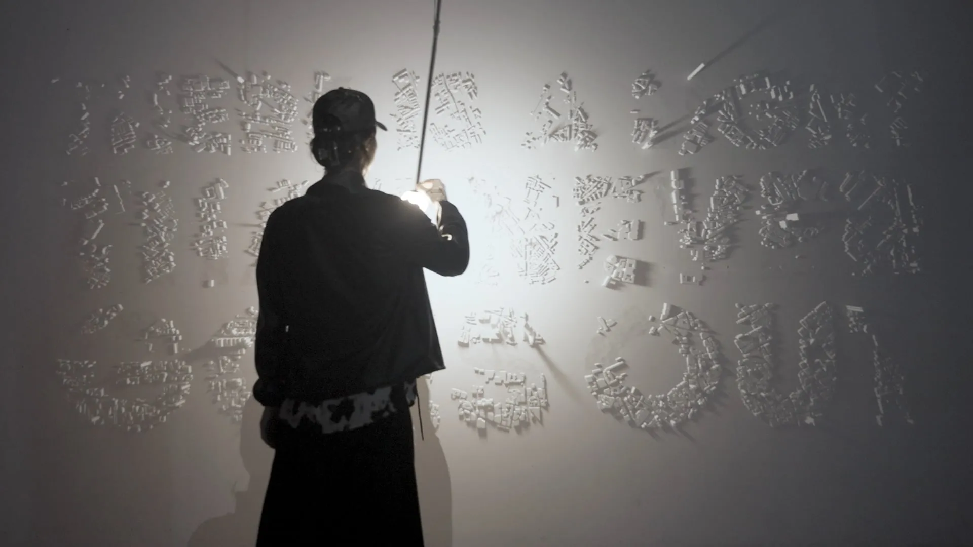 A person engages with a motion-tracked pendant lamp that controls dynamic projected shadows of letterforms, blurring digital and physical.