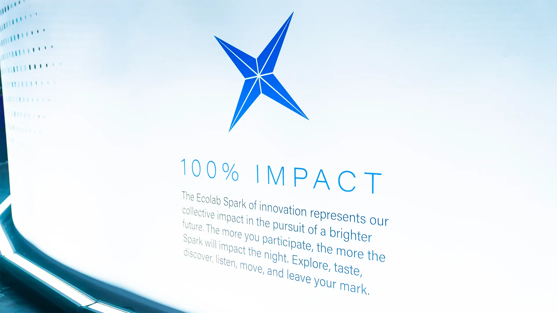 A white wall features the Ecolab logo at its center, topped with the bold header "100% IMPACT," followed by additional promotional text.