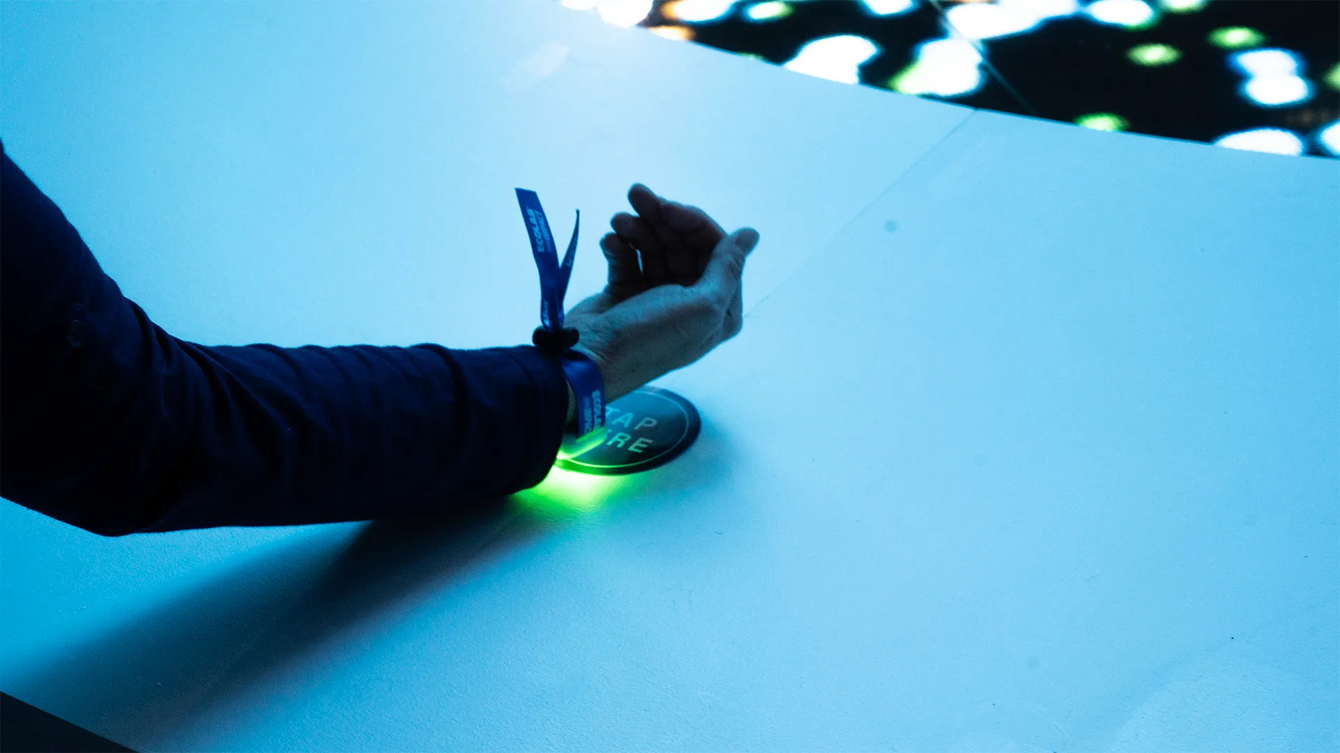 A close-up look of how a person is tapping the bracelet with a green LED light inside onto a RFID reader