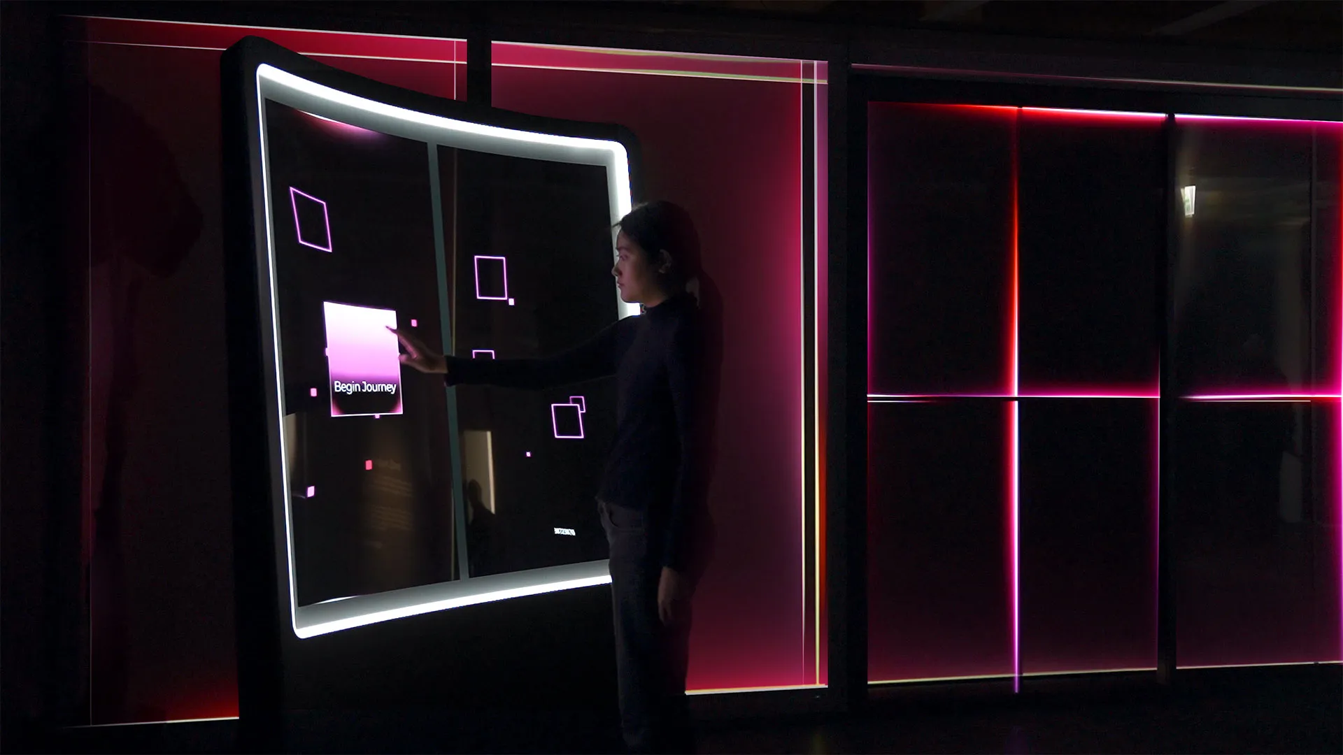 a dark room with a large interactive transparent led screen with woman interacting. begin journey text is displayed onscreen